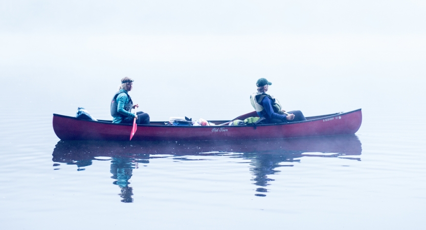 Two people navigate a canoe through fog 